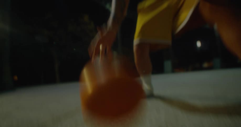 A man dribbling a basketball on an outdoor court at night
