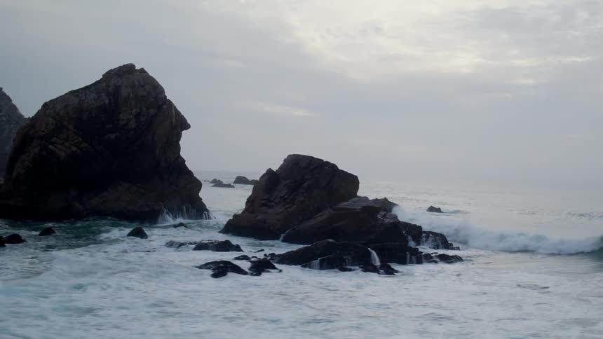 Some boulders and rocks with water along the coast with the water splashing