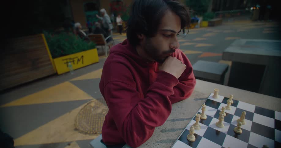 Two men play chess in a public area with people walking around