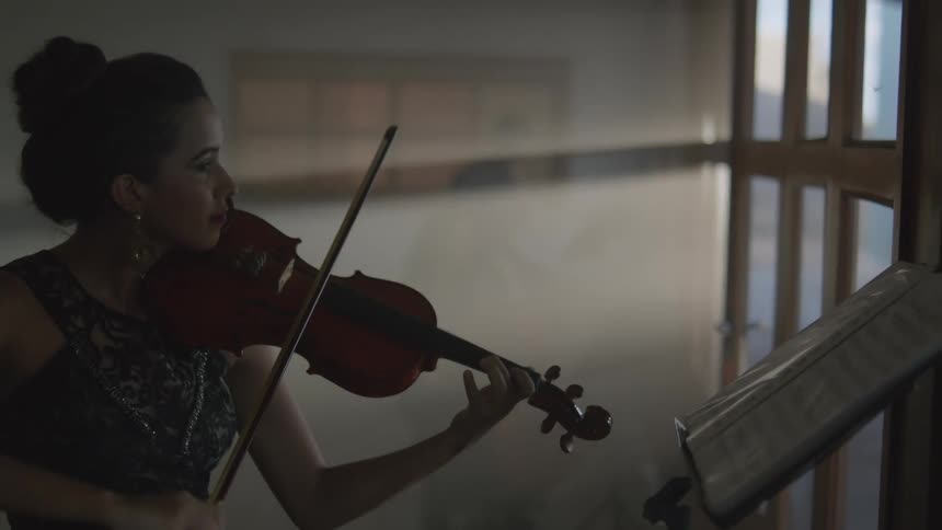 A woman is playing a violin as another woman plays a big bass guitar and a man plays a clarinet