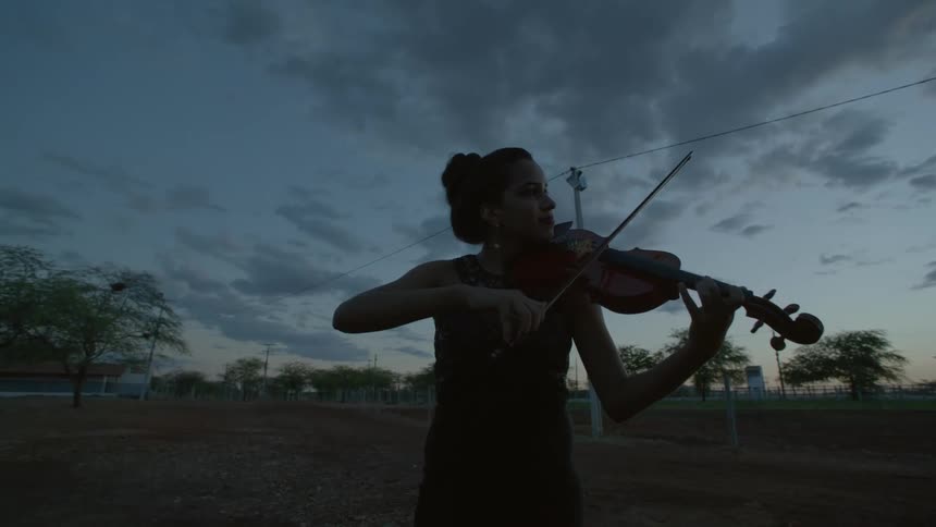 A female plays a violin outside in a field as the sun sets