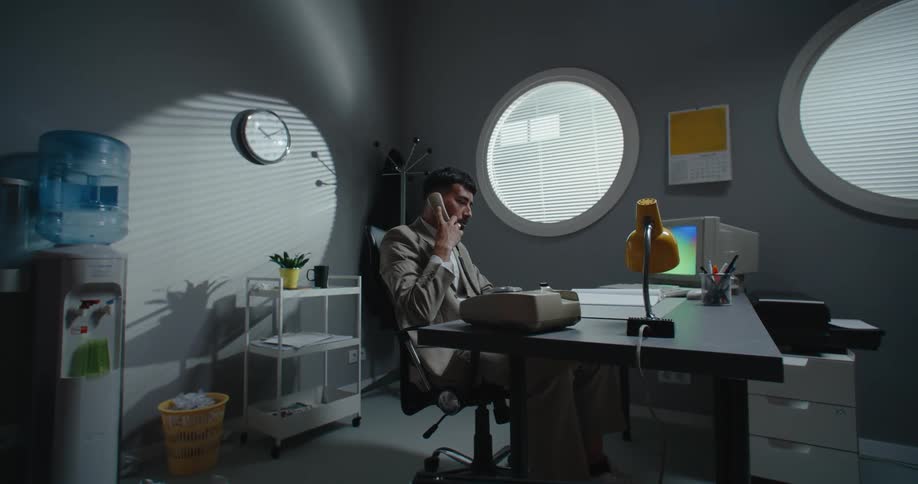 A man in an office talks on a phone and then slams it down as he hangs up