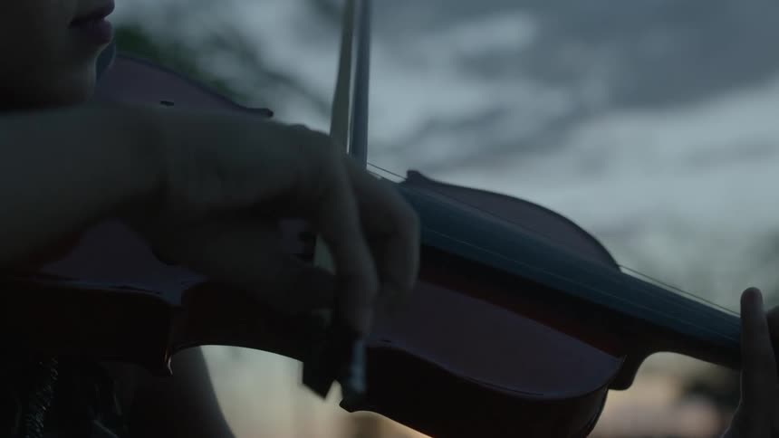 A woman moves her fingers over the strings of her violin as she moves the bow as she plays