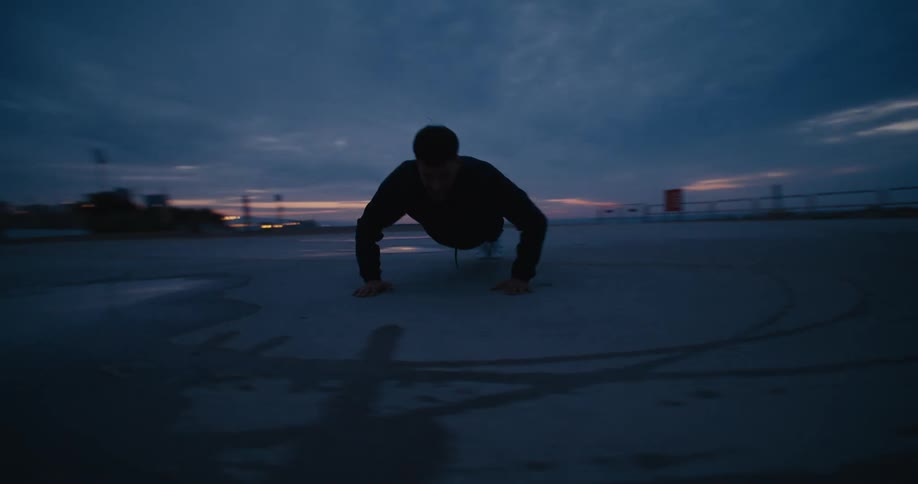 A man is outside in a park near the beach doing push ups under a cloudy sky