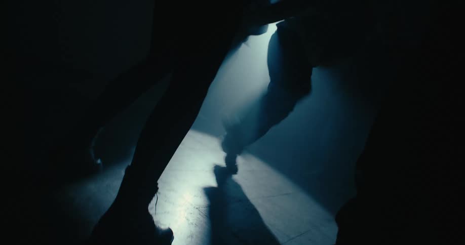 Silhouettes of men dancing around a man break dancing on the floor as a light shines upon them