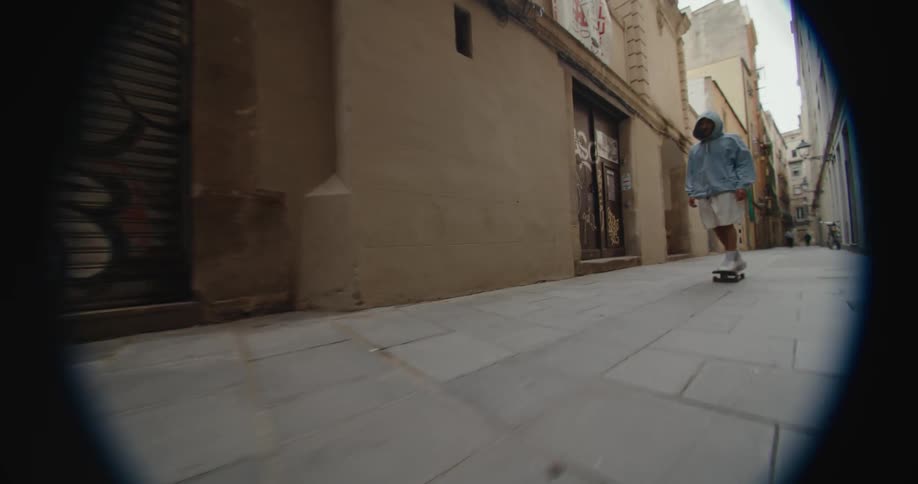 Young man wearing a hoodie rides a skateboard on a narrow city street