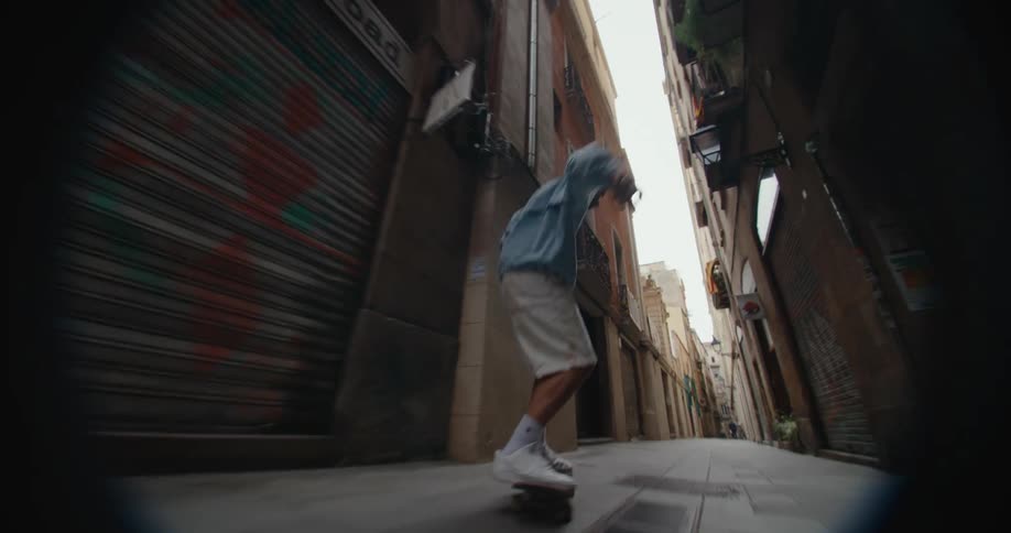 Young man wearing a hoodie rides a skateboard on a narrow city alley