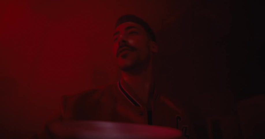 A man is walking in a room illuminated with red light and a mirrored disco ball on the ceiling