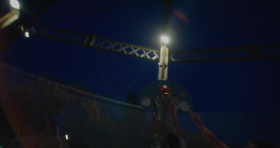 Man scores a basket on an outdoor basketball court at night while three other men try to stop him