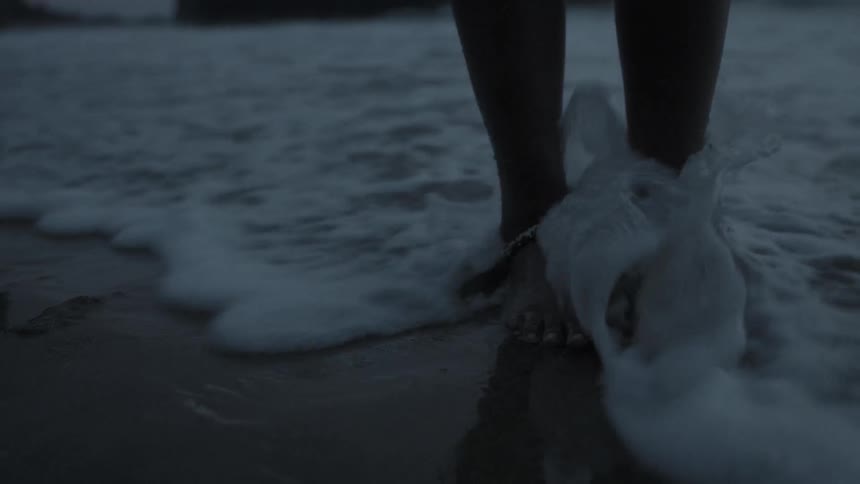 A person moves their feet in the sand as waves go over them