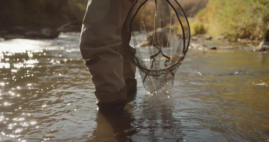 Man with gray pants and fishing net stands in the stream