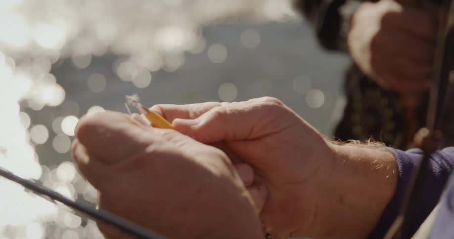 A man threads fishing line through a loop to attach a fly lure