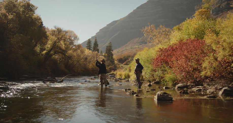 Men wearing hats black coats and pants fish in the forest stream