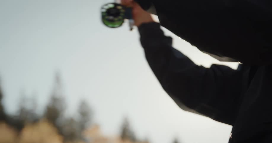 Man wearing black jacket casts fishing rod in the river