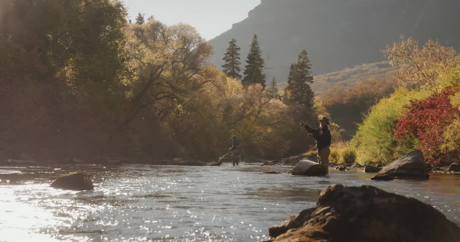 A man throws a fishing line into the river while standing on rocks