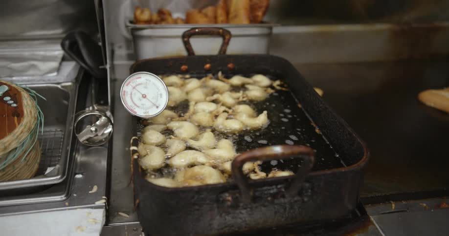 Thermometer measuring the temperature of cooking oil while frying dumplings