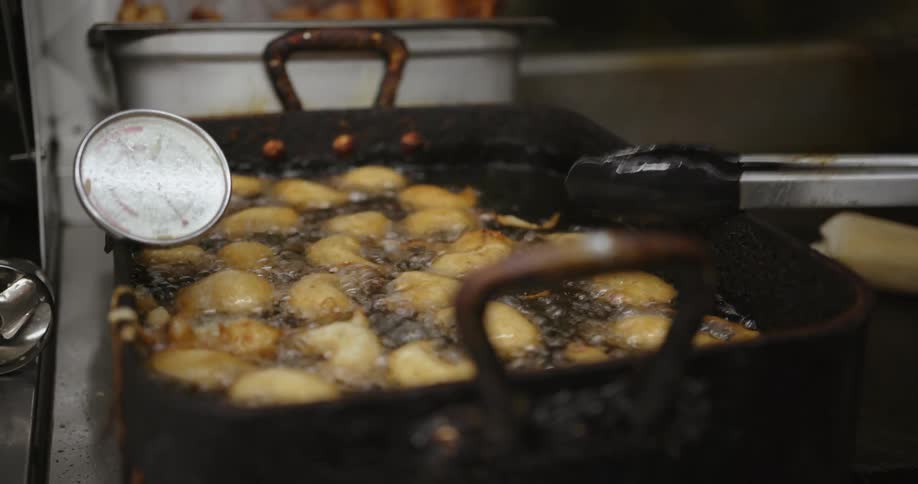 A person uses a pair of tongs to rearrange food in a deep fryer