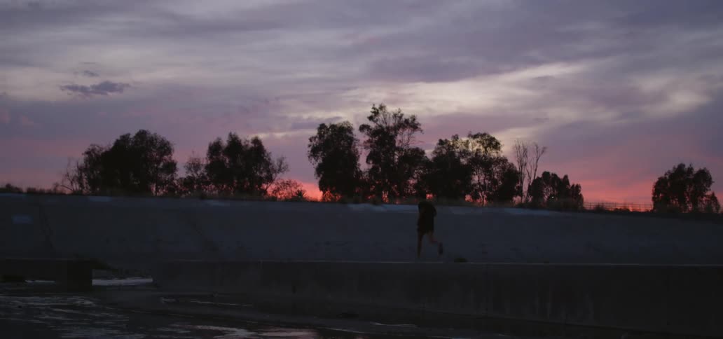 The silhouette of a young man running across a cement barrier at sunset
