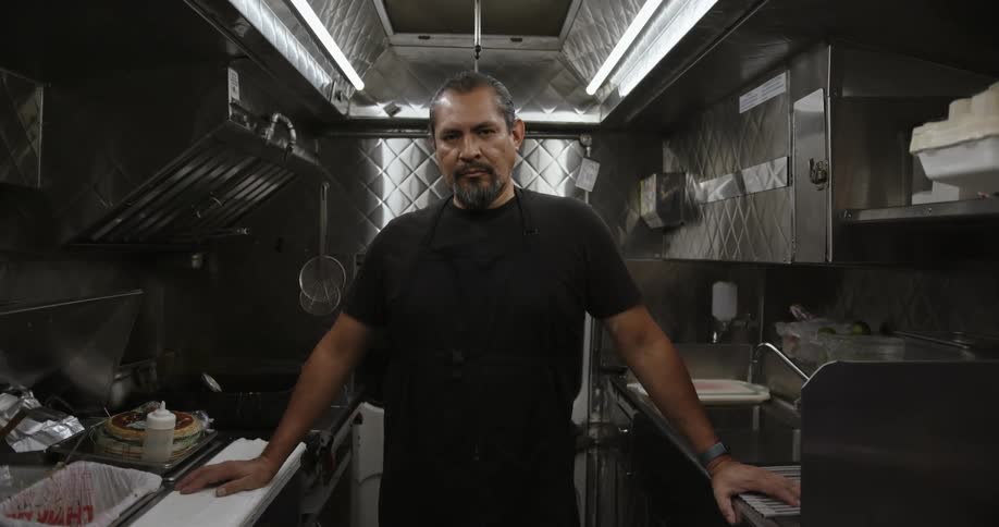 Man poses standing in narrow stainless steel kitchen
