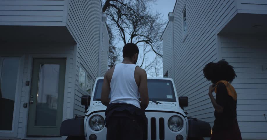 Two people talk in front of the vehicle