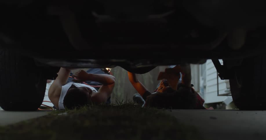 A man and woman talk while working underneath a car
