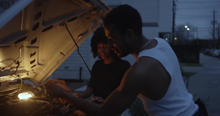 A man and a woman are outside working under the hood of their automobile checking the fluids