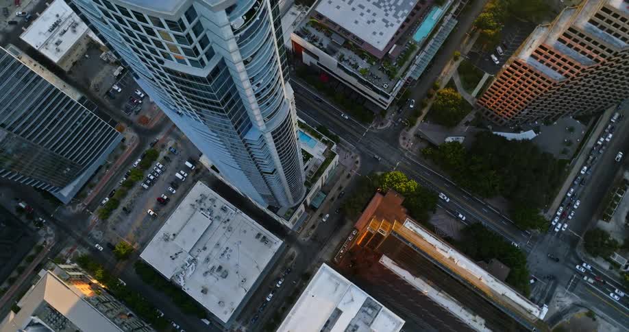 Looking down at traffic moving on downtown streets around a tall skyscraper and neighboring buildings