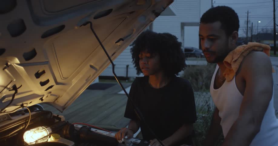 Two people are talking and smiling as they look at the engine of a car