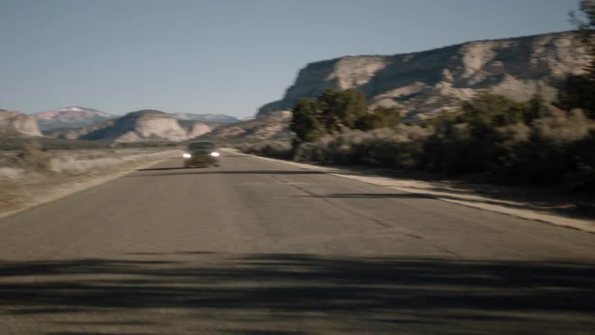 A car is driving down the road with a mountain behind