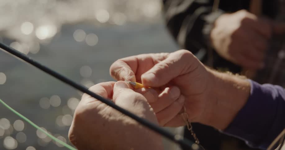 Close up of mans hands adjusting fishing line near the gleaming water