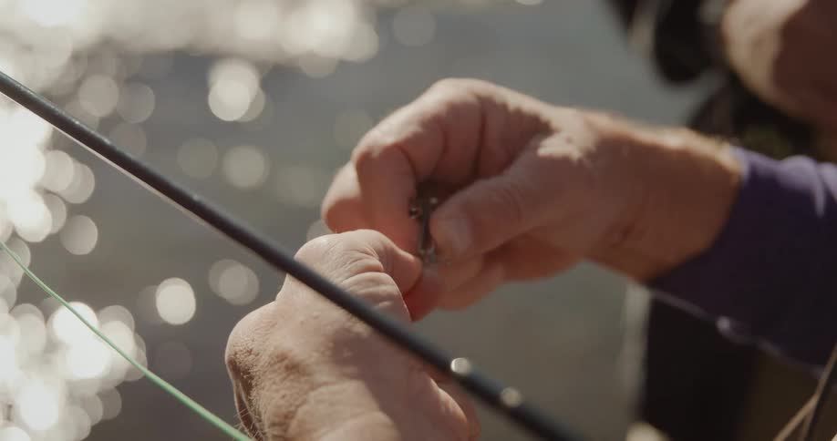 A fisherman shields his eyes with a visor while tying bait to fishing wire