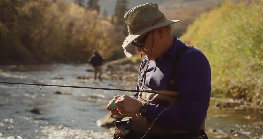 Man threading a fishing line while standing on a river at morning