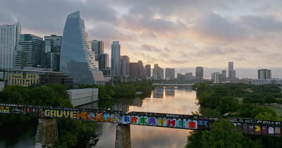 Aerial view of a bridge decorated in colorful graffiti over a river in the city at evening