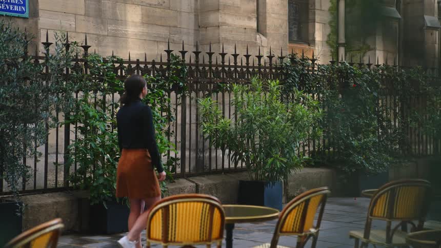 A woman is walking on a sidewalk that has several tables and chairs set up