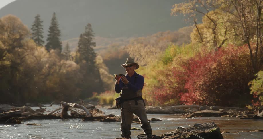 A man is holding a fish on the river during dusk