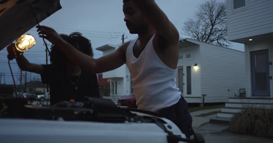 Man with white undershirt opens white jeeps hood in the street