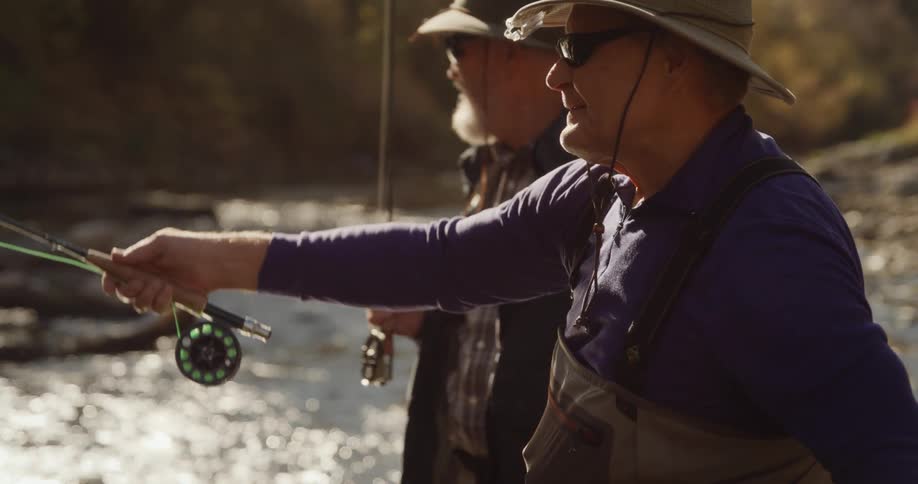 Two men who look related are getting their fishing poles ready to fish in a river