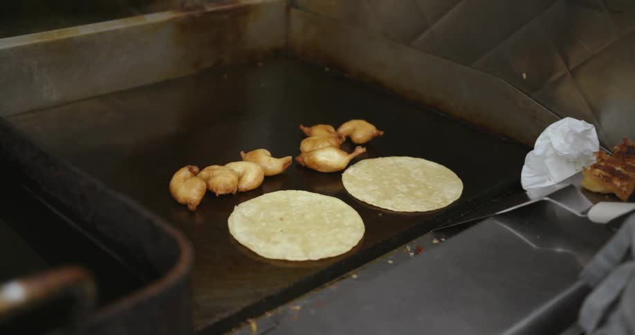 A person in the kitchen is cooking lamb chops with pita bread on a flat topped grill