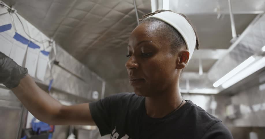 Woman with white headband black shirt and gloves cooks food in the kitchen