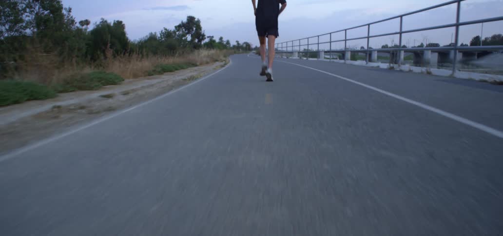 Youth runs along asphalt paved track near large storm drain