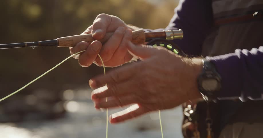 Man wit purple sweater gray pants an wristwatch pulls fishing line in the forest stream