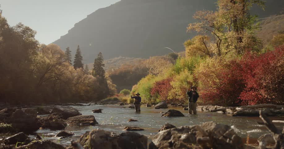 Two people are fishing on a river during dusk