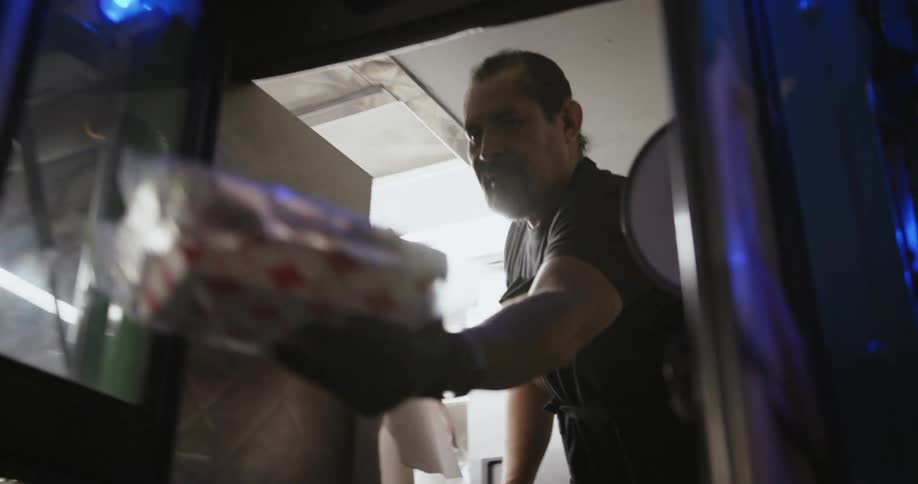 Man with goatee black apron and shirt give a takeaway to the customer in food truck at night