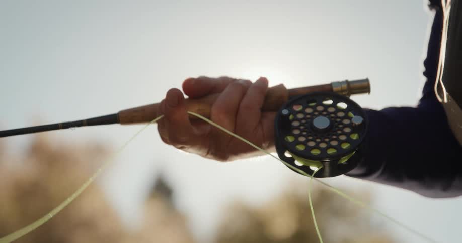 Sun glares down as man pulls fishing line while holding fishing rod