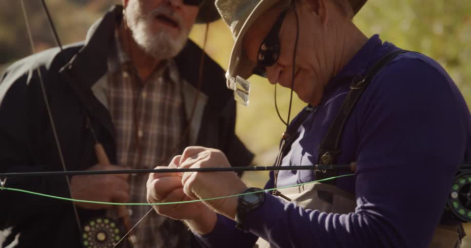 Elderly man with wearing sunglasses and hat hook a piece of bait on fishing poles hook