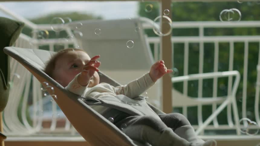 Baby lying in baby bouncer looks up at bubbles in room