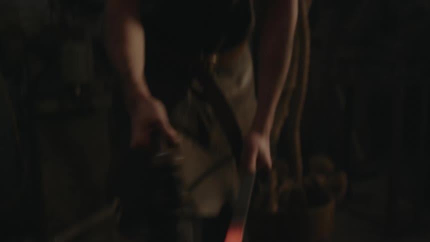 A blacksmith is striking a piece of molten hot metal with a hammer as it glows on the anvil