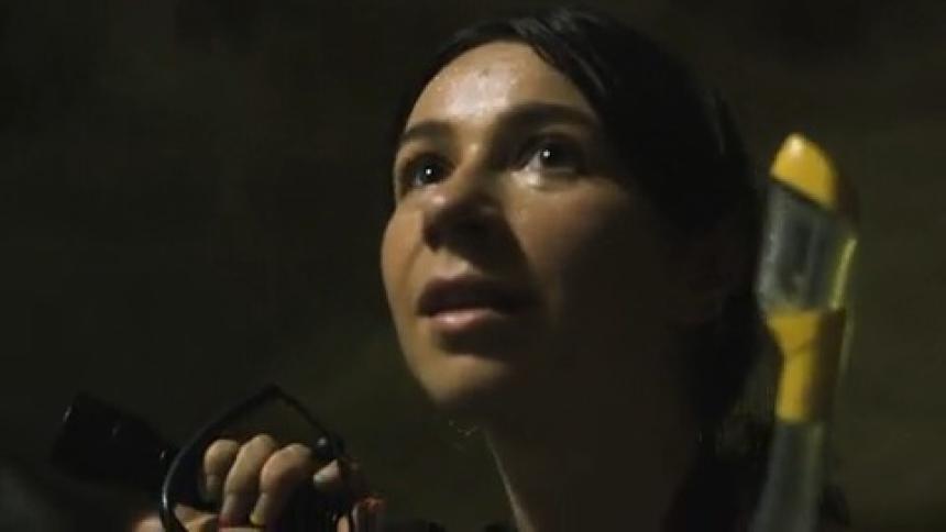 A woman with a snorkeling mask looking around a cave with a flashlight