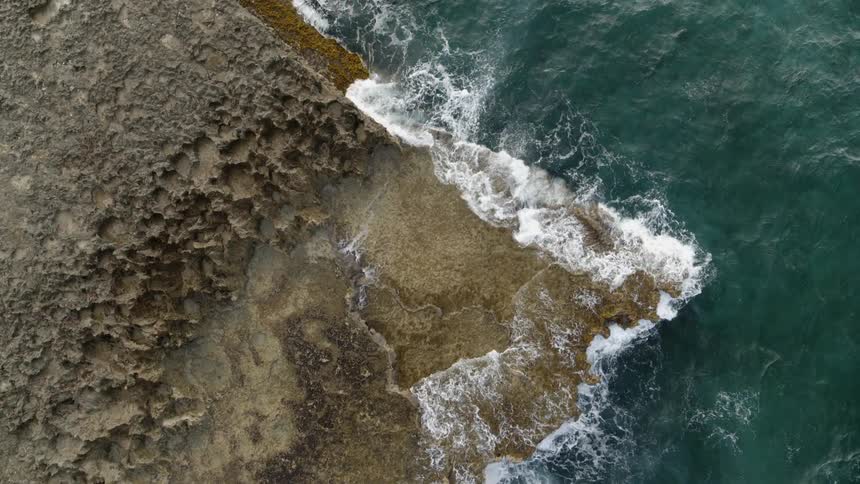 Turquoise water crashes against a sculpted volcanic rock ledge