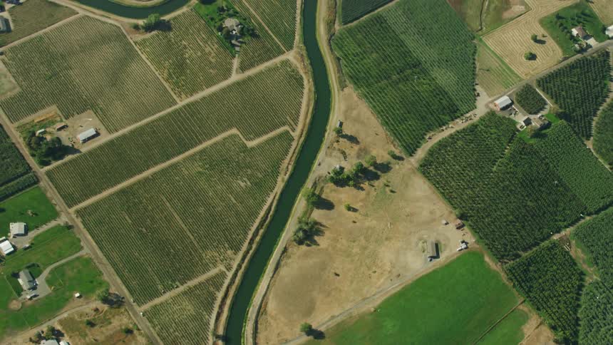 High altitude aerial looking down on irrigation canals as they run and weave through a orchards, agricultural land and various farms and ranches
